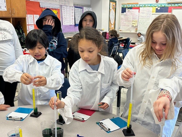 Students in white lab coats conducting an experiment